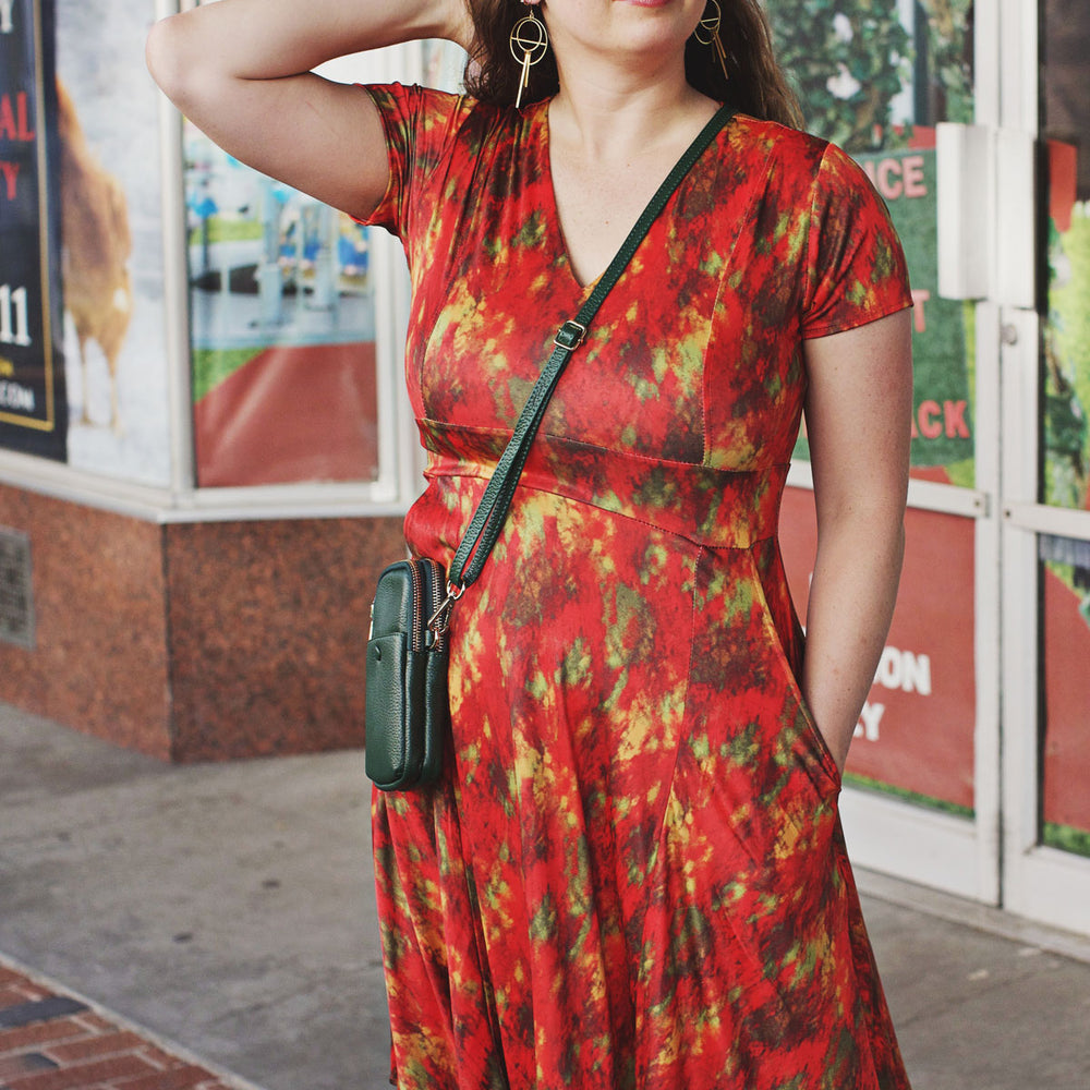 
                  
                    Woman wearing a red abstract dress with a forest green shoulder bag in front of a store.
                  
                