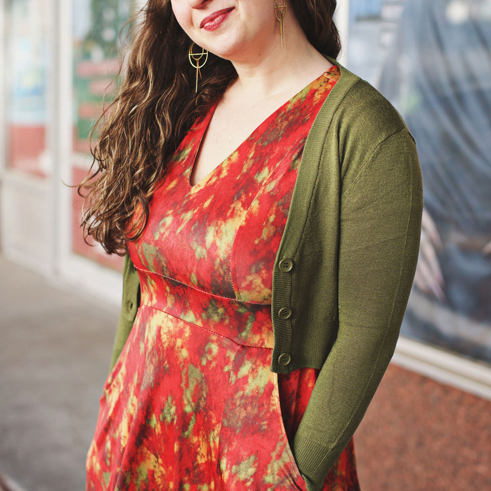 Woman wearing a red abstract print dress with an olive green cardigan standing outdoors.