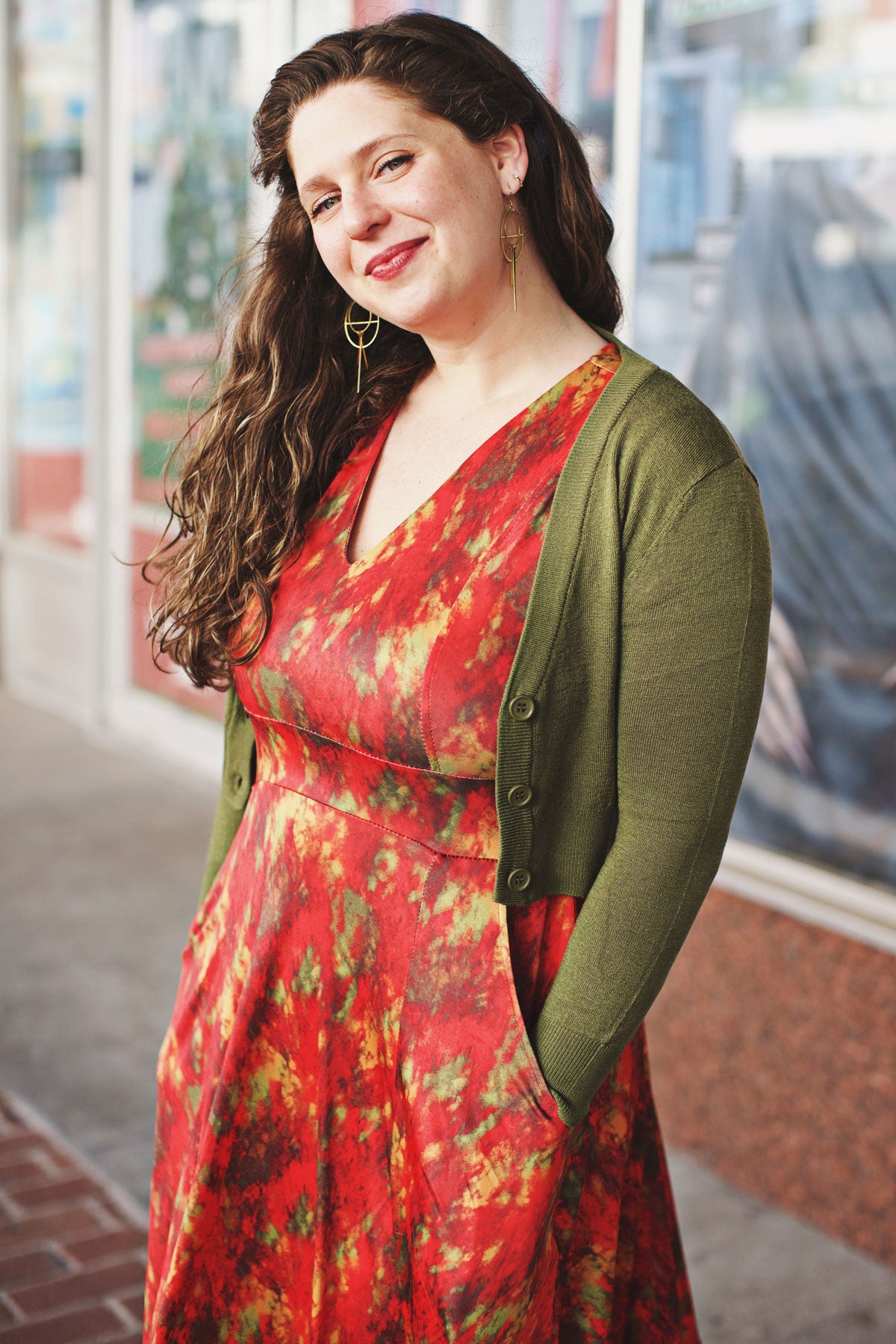Woman wearing a red abstract print dress with an olive green cardigan standing outdoors.