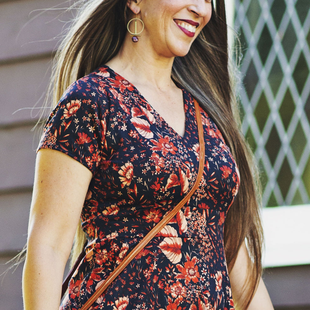 Woman wearing a floral dress with a brown crossbody bag, standing outdoors.