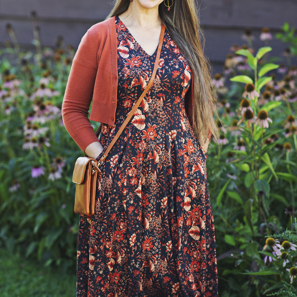 
                  
                    Woman wearing a floral dress and burnt orange cardigan standing in a garden.
                  
                