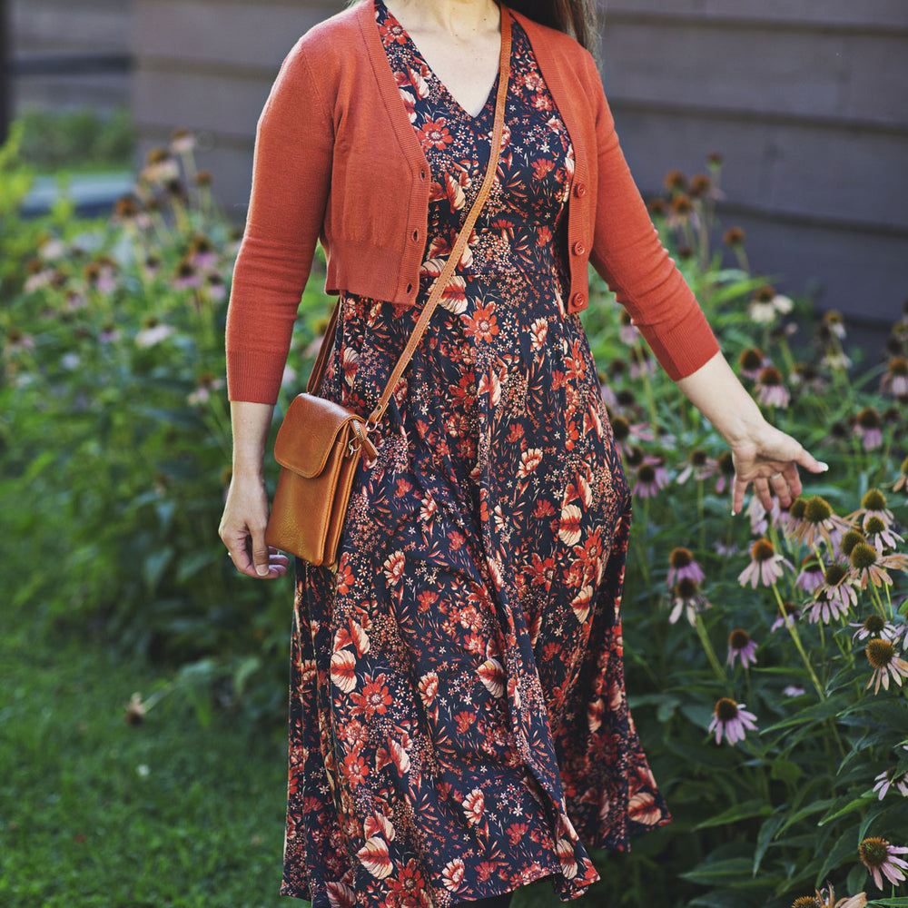
                  
                    Woman wearing a floral dress and burnt orange cardigan standing in a garden.
                  
                