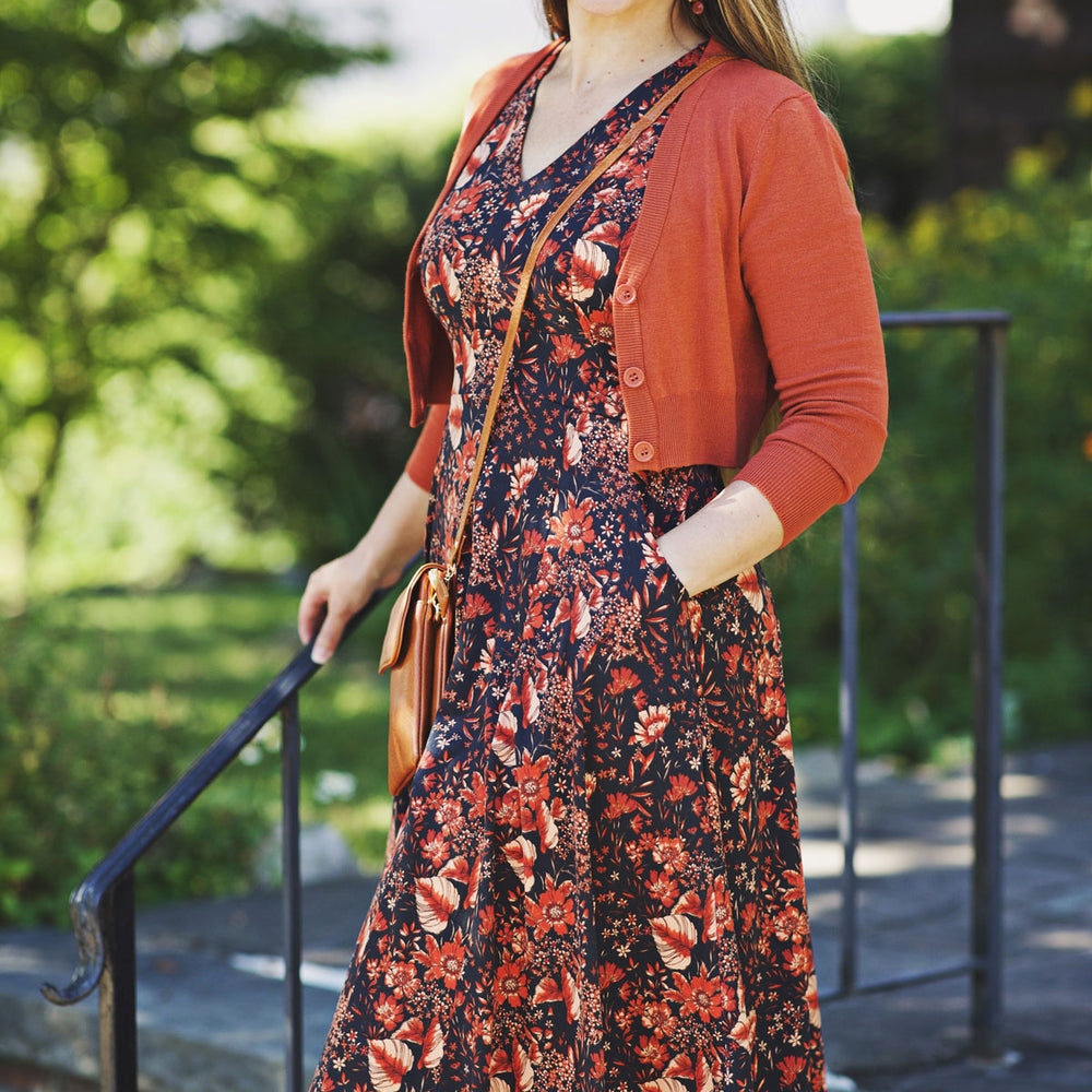 Woman wearing a floral dress and burnt orange cardigan standing in a city.