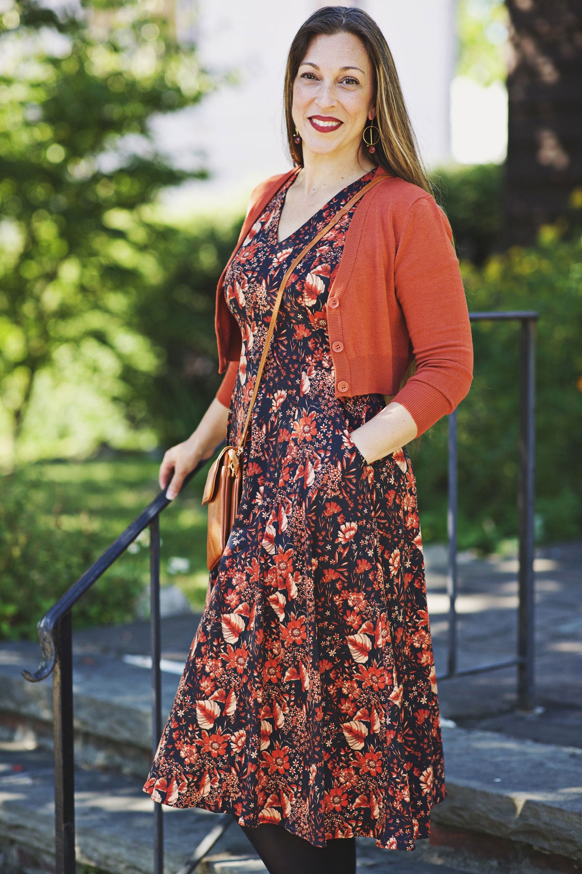 Woman wearing a floral dress and burnt orange cardigan standing in a city.