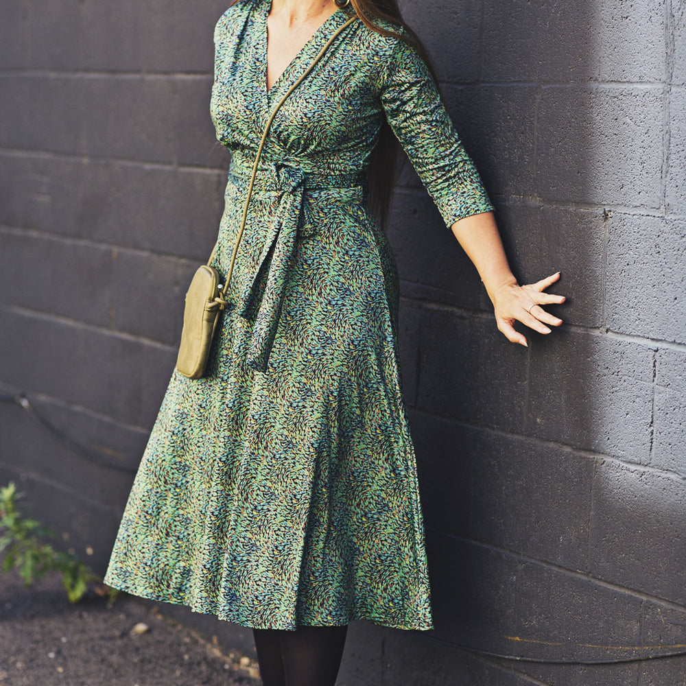 Woman in a green dress standing against a dark brick wall.