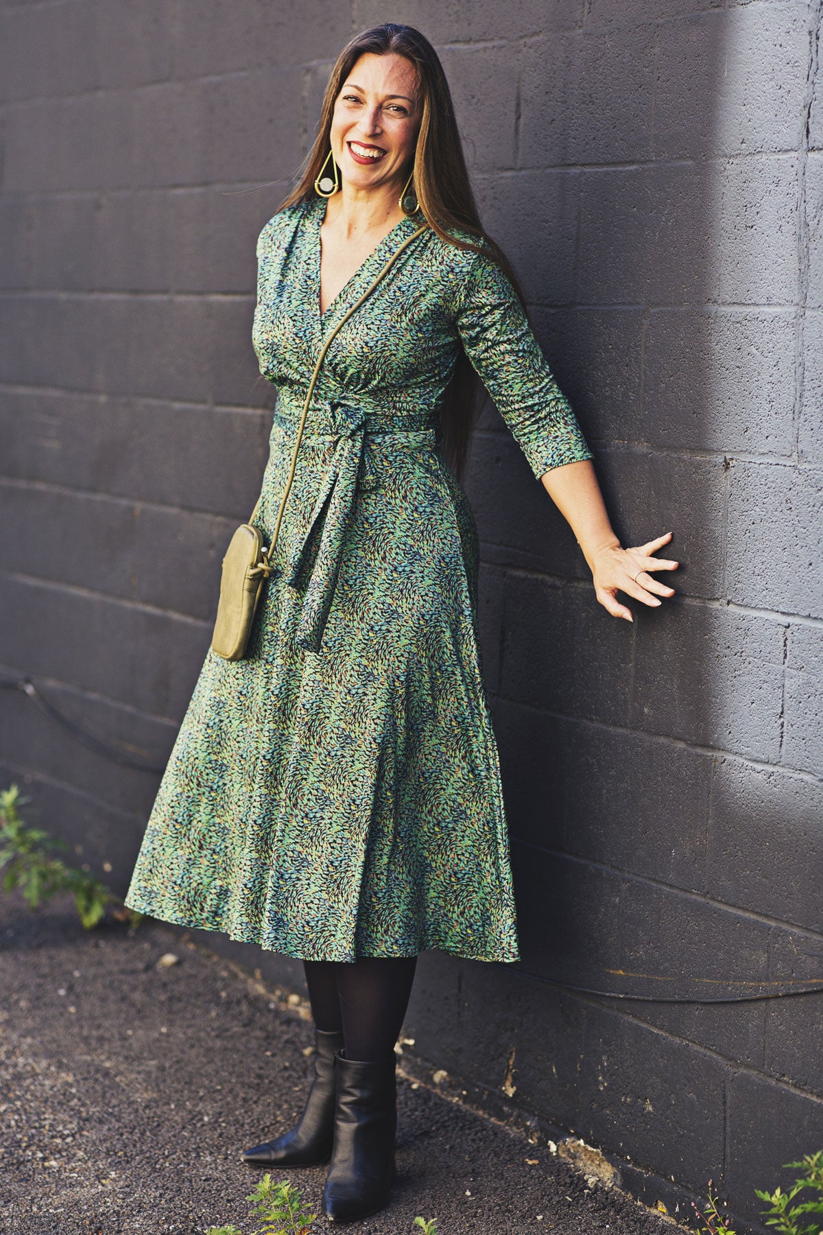 Woman in a green dress standing against a dark brick wall.