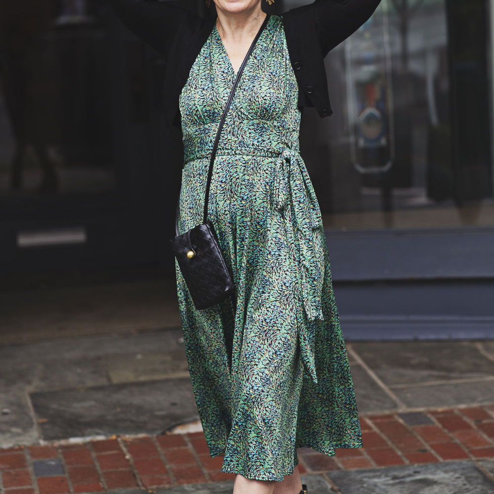 
                  
                    Woman in a green dress with a black cardigan and boots standing on a street.
                  
                