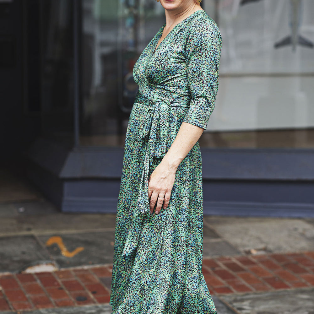 
                  
                    Woman wearing a green patterned dress standing on a street.
                  
                